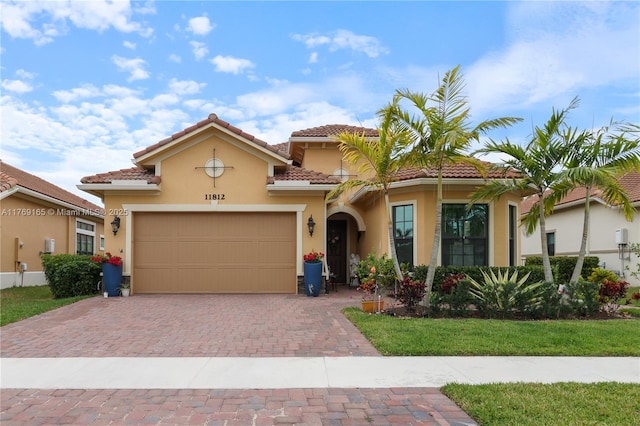 mediterranean / spanish-style home with an attached garage, a tiled roof, stucco siding, and decorative driveway