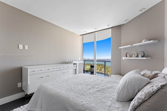 bedroom with a wall of windows, visible vents, baseboards, and a water view