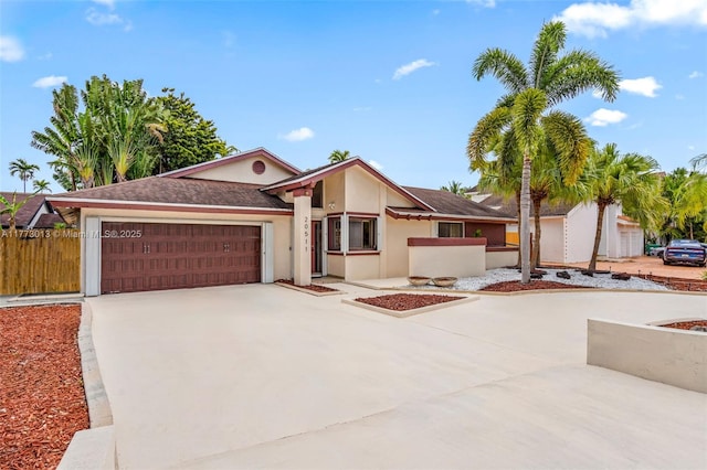 view of front facade with stucco siding, a garage, fence, and driveway
