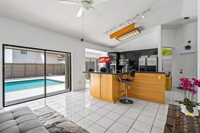 kitchen with dark countertops, track lighting, a kitchen breakfast bar, stainless steel appliances, and a ceiling fan