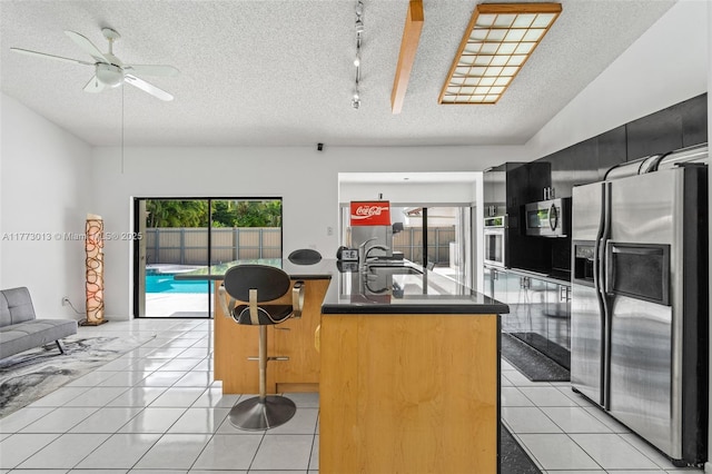 kitchen featuring appliances with stainless steel finishes, a sink, a textured ceiling, light tile patterned floors, and a center island with sink