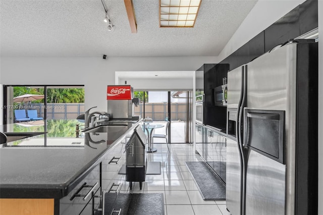 kitchen with a textured ceiling, a sink, light tile patterned floors, dark cabinets, and stainless steel appliances
