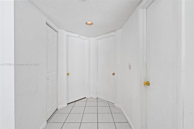 hallway with baseboards, a textured ceiling, and light tile patterned floors