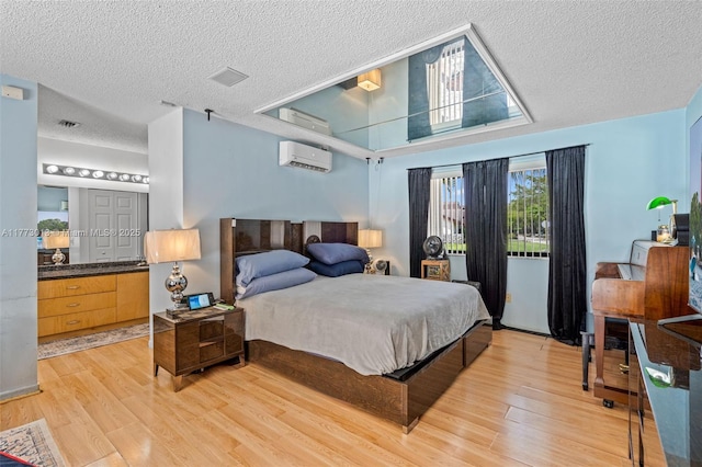 bedroom with a textured ceiling, light wood finished floors, and a wall mounted air conditioner