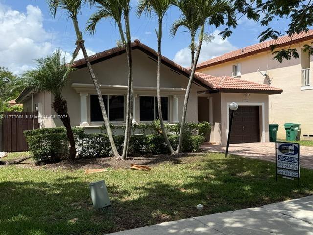view of front of home featuring driveway, a front yard, stucco siding, a tiled roof, and a garage