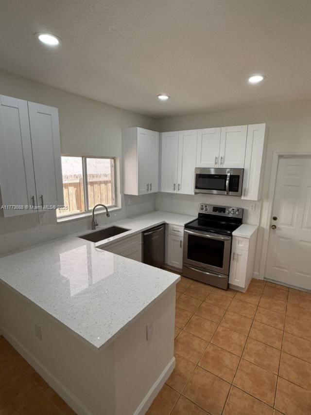 kitchen featuring white cabinets, a peninsula, appliances with stainless steel finishes, a sink, and light tile patterned floors