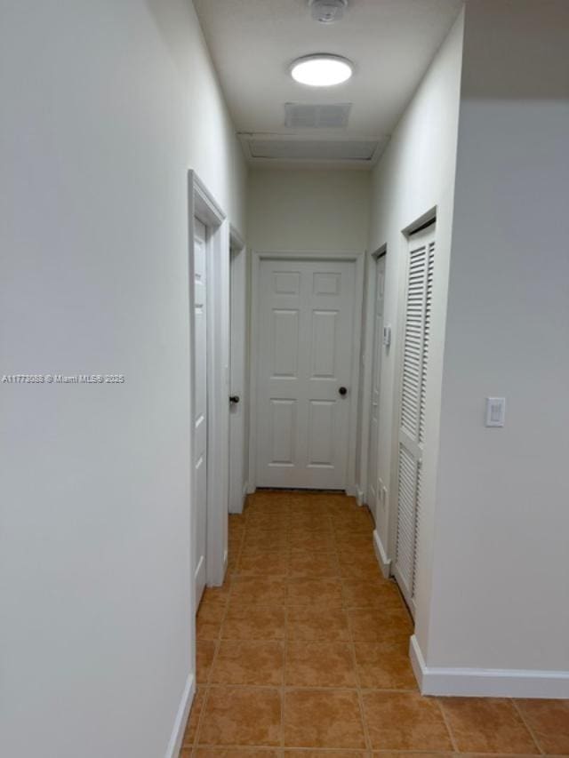 corridor featuring baseboards, visible vents, and light tile patterned floors
