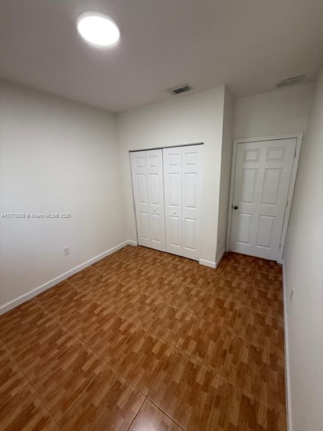 unfurnished bedroom featuring baseboards, visible vents, a closet, and wood finished floors