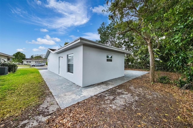 view of property exterior with central AC, stucco siding, and a lawn