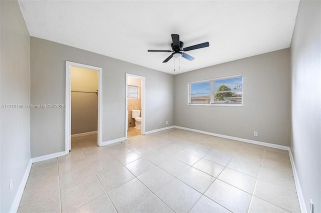 unfurnished bedroom with a closet, baseboards, a ceiling fan, light tile patterned flooring, and a walk in closet