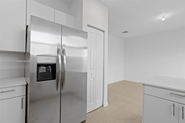 kitchen with stainless steel refrigerator with ice dispenser, light tile patterned floors, visible vents, white cabinets, and light stone countertops