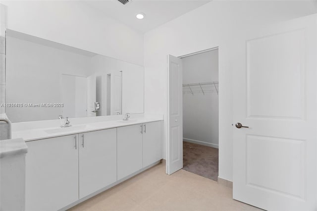 full bathroom with double vanity, a walk in closet, baseboards, and a sink