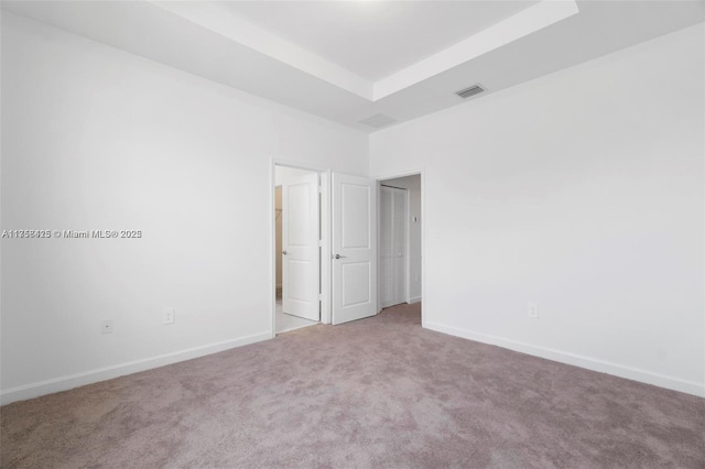 empty room with baseboards, a tray ceiling, carpet, and visible vents