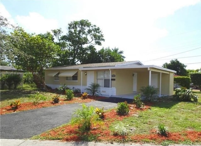 ranch-style home featuring a front lawn, an attached carport, stucco siding, and aphalt driveway