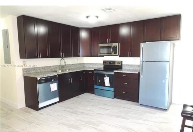 kitchen featuring visible vents, electric panel, stainless steel appliances, a sink, and light stone counters