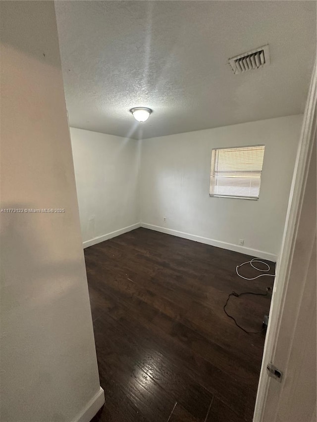 spare room featuring baseboards, a textured ceiling, dark wood-style floors, and visible vents