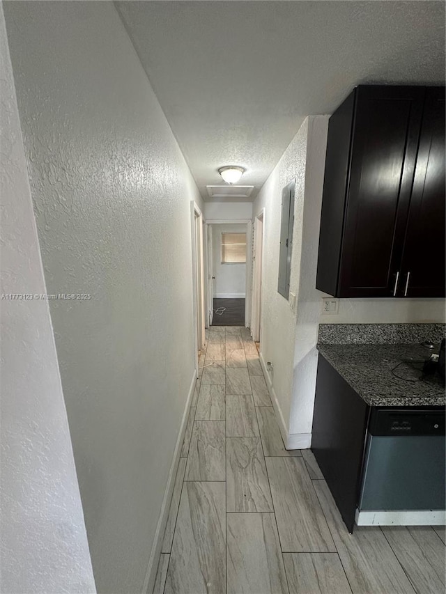 hall featuring baseboards, a textured ceiling, a textured wall, and electric panel
