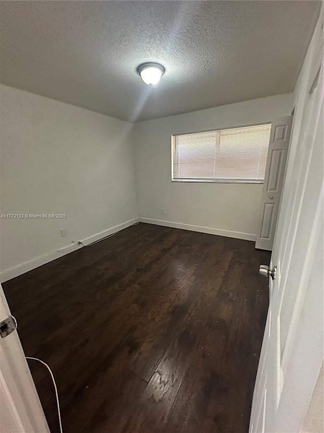 spare room featuring baseboards, a textured ceiling, and dark wood-style flooring