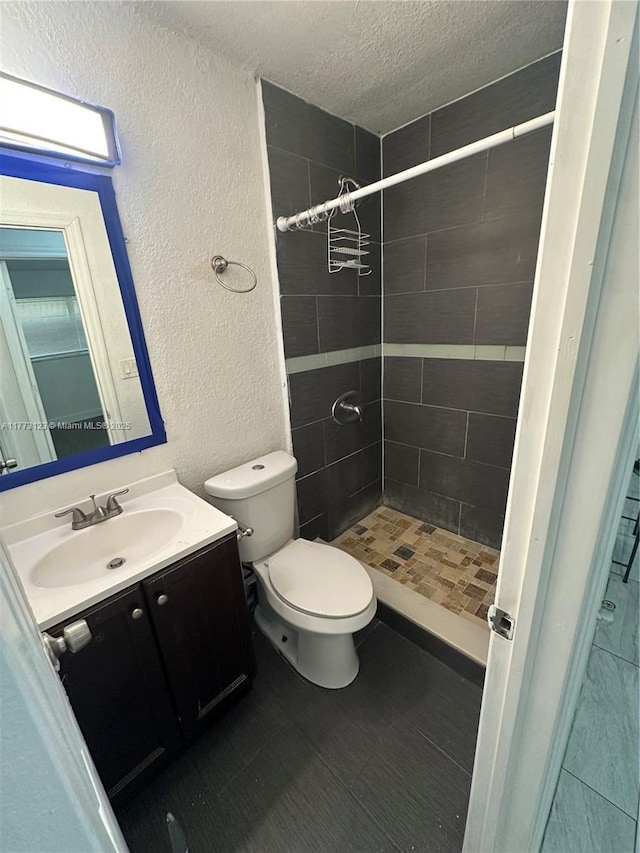 bathroom with toilet, vanity, a shower stall, a textured ceiling, and a textured wall