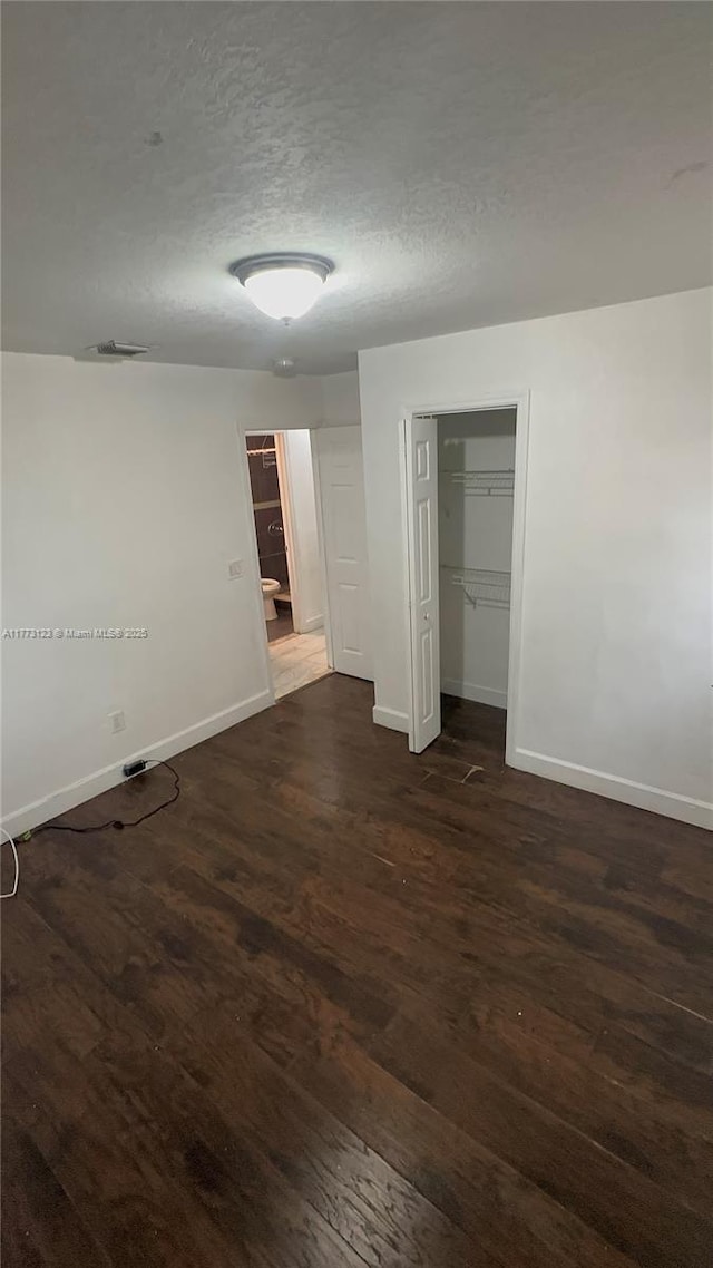 spare room with a textured ceiling, visible vents, baseboards, and dark wood-style flooring
