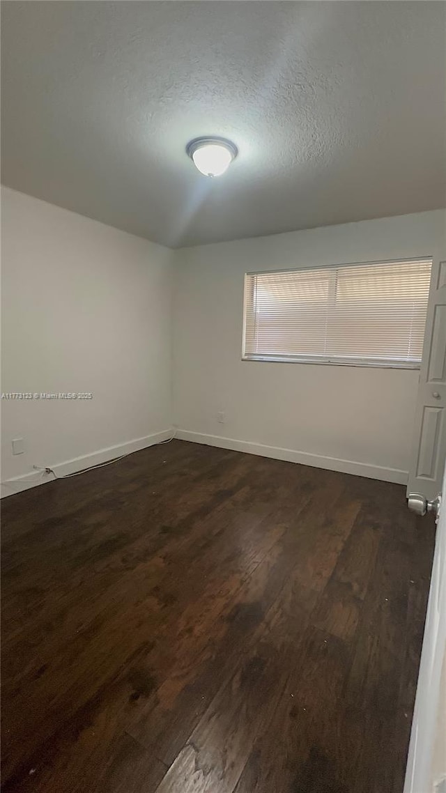 unfurnished room with dark wood-type flooring, baseboards, and a textured ceiling