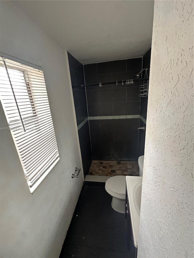 bathroom with a textured wall, toilet, a tile shower, and vanity