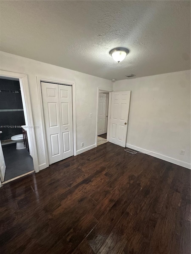 unfurnished bedroom featuring baseboards, dark wood-style flooring, a textured ceiling, and a closet