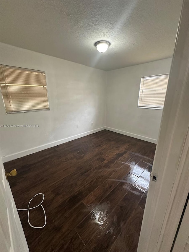 unfurnished room with baseboards, a textured ceiling, and dark wood-style flooring