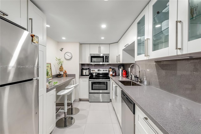 kitchen with light stone countertops, tasteful backsplash, a sink, light tile patterned floors, and stainless steel appliances