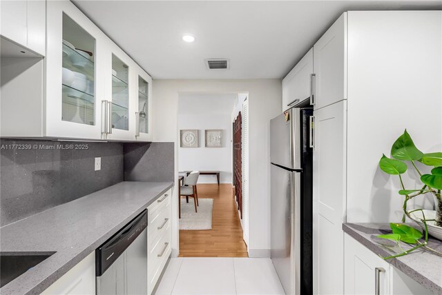 kitchen with appliances with stainless steel finishes, white cabinetry, backsplash, visible vents, and glass insert cabinets