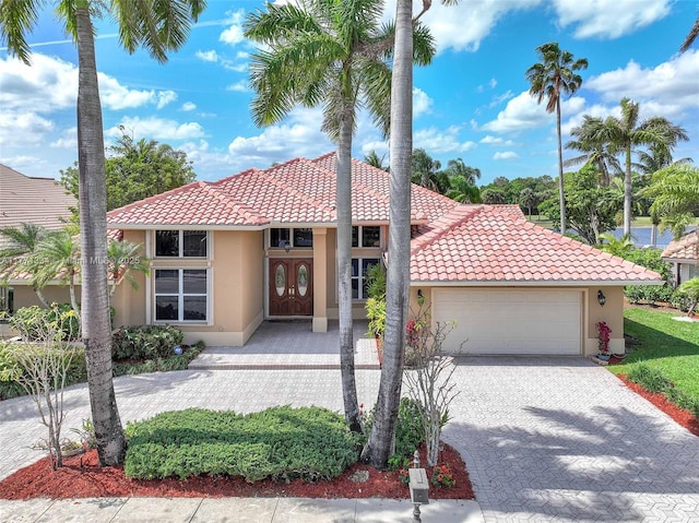 mediterranean / spanish home featuring decorative driveway, a tile roof, stucco siding, and an attached garage