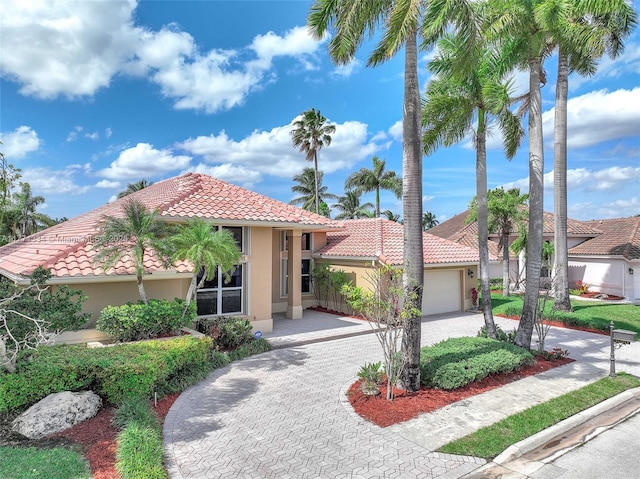 mediterranean / spanish-style home featuring a tiled roof, decorative driveway, stucco siding, and an attached garage
