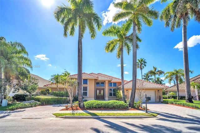 mediterranean / spanish-style home with a tile roof, decorative driveway, stucco siding, and an attached garage