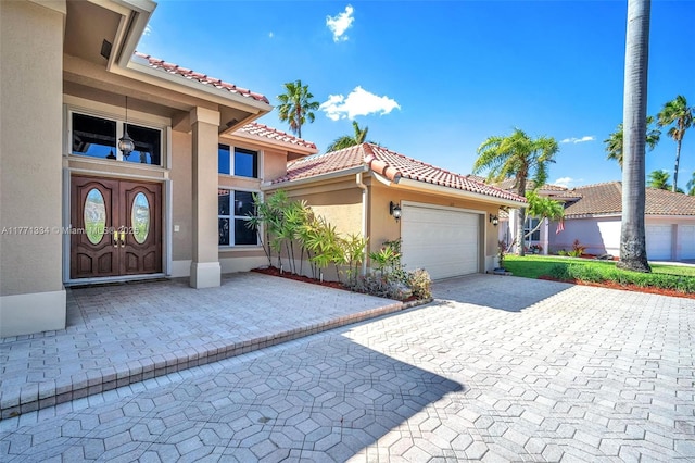 exterior space featuring stucco siding, an attached garage, a tiled roof, and decorative driveway