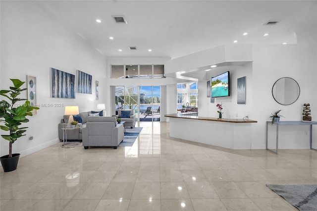 living area featuring baseboards, a towering ceiling, visible vents, and crown molding