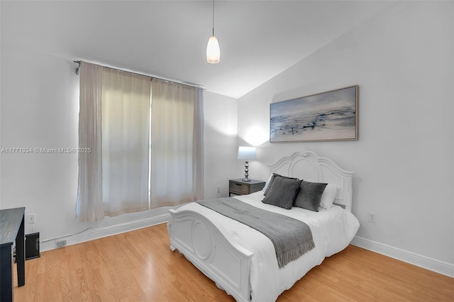 bedroom with baseboards, light wood-type flooring, and lofted ceiling