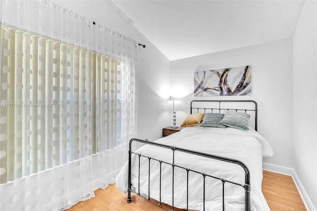 bedroom with baseboards, lofted ceiling, and wood finished floors