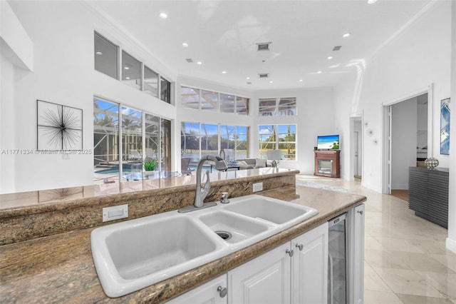 kitchen with white cabinetry, a sink, a towering ceiling, and beverage cooler