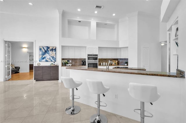 kitchen featuring a high ceiling, visible vents, a kitchen breakfast bar, and crown molding