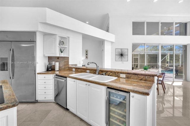 kitchen featuring a sink, tasteful backsplash, appliances with stainless steel finishes, a peninsula, and beverage cooler