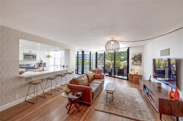 living room with light wood-type flooring, an inviting chandelier, baseboards, floor to ceiling windows, and wallpapered walls