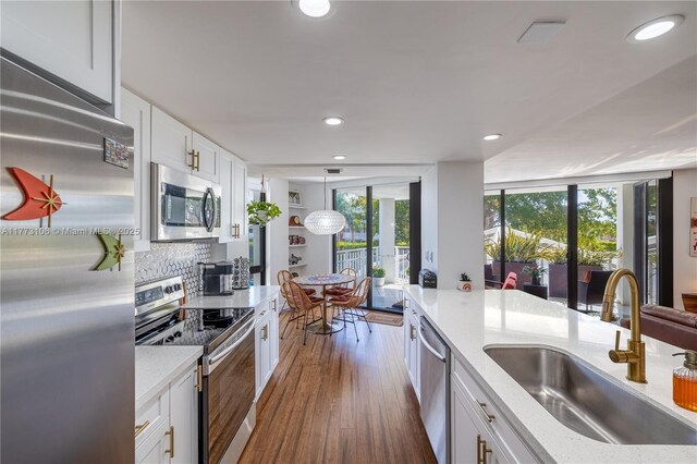 kitchen with a sink, dark wood-style floors, light stone counters, white cabinets, and appliances with stainless steel finishes