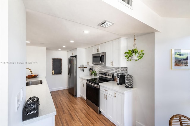 kitchen featuring tasteful backsplash, a sink, visible vents, light wood-style flooring, and appliances with stainless steel finishes