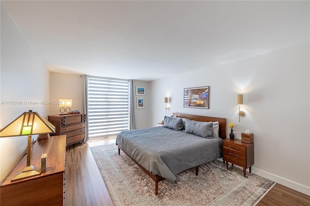 bedroom featuring baseboards, a wall of windows, and wood finished floors