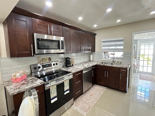 kitchen featuring stainless steel appliances, light stone countertops, a sink, and backsplash