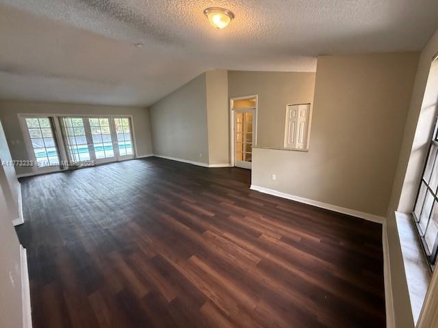 unfurnished living room with baseboards, lofted ceiling, a textured ceiling, and dark wood-style flooring