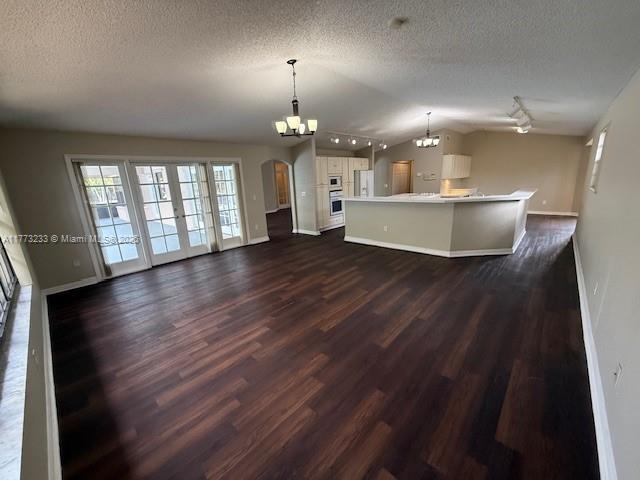 unfurnished living room featuring dark wood-style flooring, plenty of natural light, arched walkways, lofted ceiling, and a notable chandelier