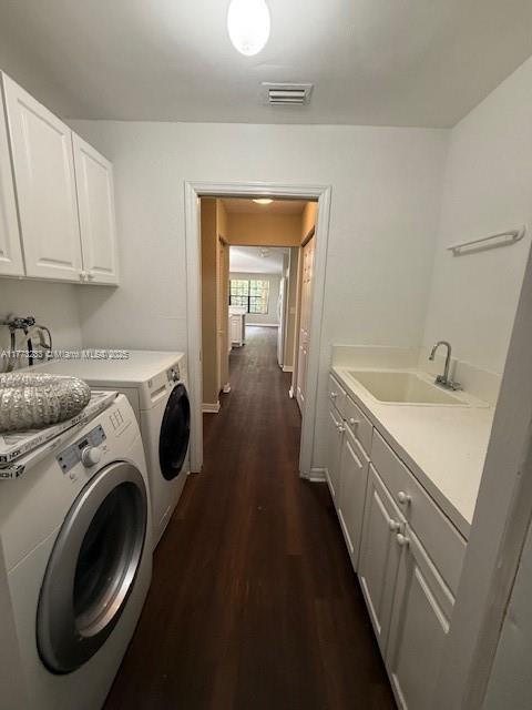 clothes washing area featuring washing machine and clothes dryer, visible vents, dark wood finished floors, a sink, and cabinet space