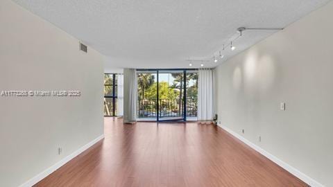 unfurnished room featuring a wall of windows, rail lighting, baseboards, wood finished floors, and visible vents