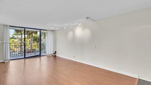 unfurnished room with baseboards, a wall of windows, and wood finished floors